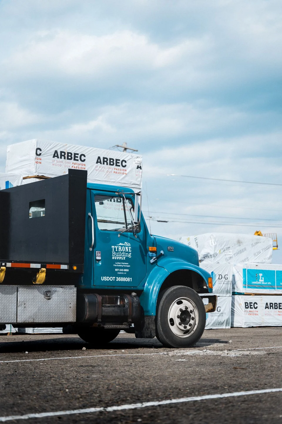 Blue Tyrone Building Supply delivery truck beside wrapped building materials