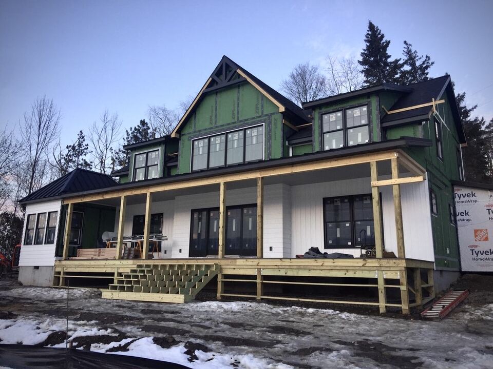 Two-story house under construction with green sheathing and a covered front porch