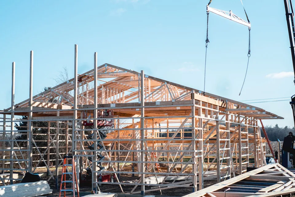 Crane installing roof trusses on a pole barn frame